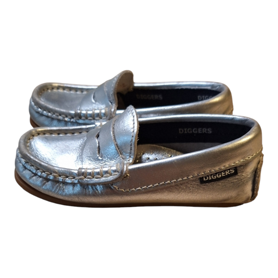A pair of Diggers Leather Moccasins in silver, size 24. The moccasins are made of shiny silver leather with visible stitching. They have a dark brown grip rubber sole.