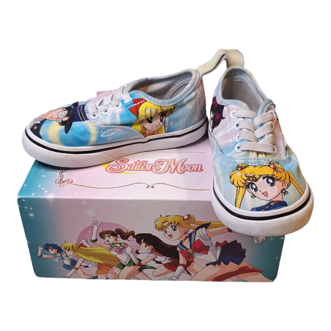  A pair of Vans x Sailor Moon Authentic Elas sneakers, size 24. The shoes feature a light blue background with Sailor Moon character artwork. They have white laces and a white rubber sole, and are displayed on top of their original box, which also features Sailor Moon artwork.
